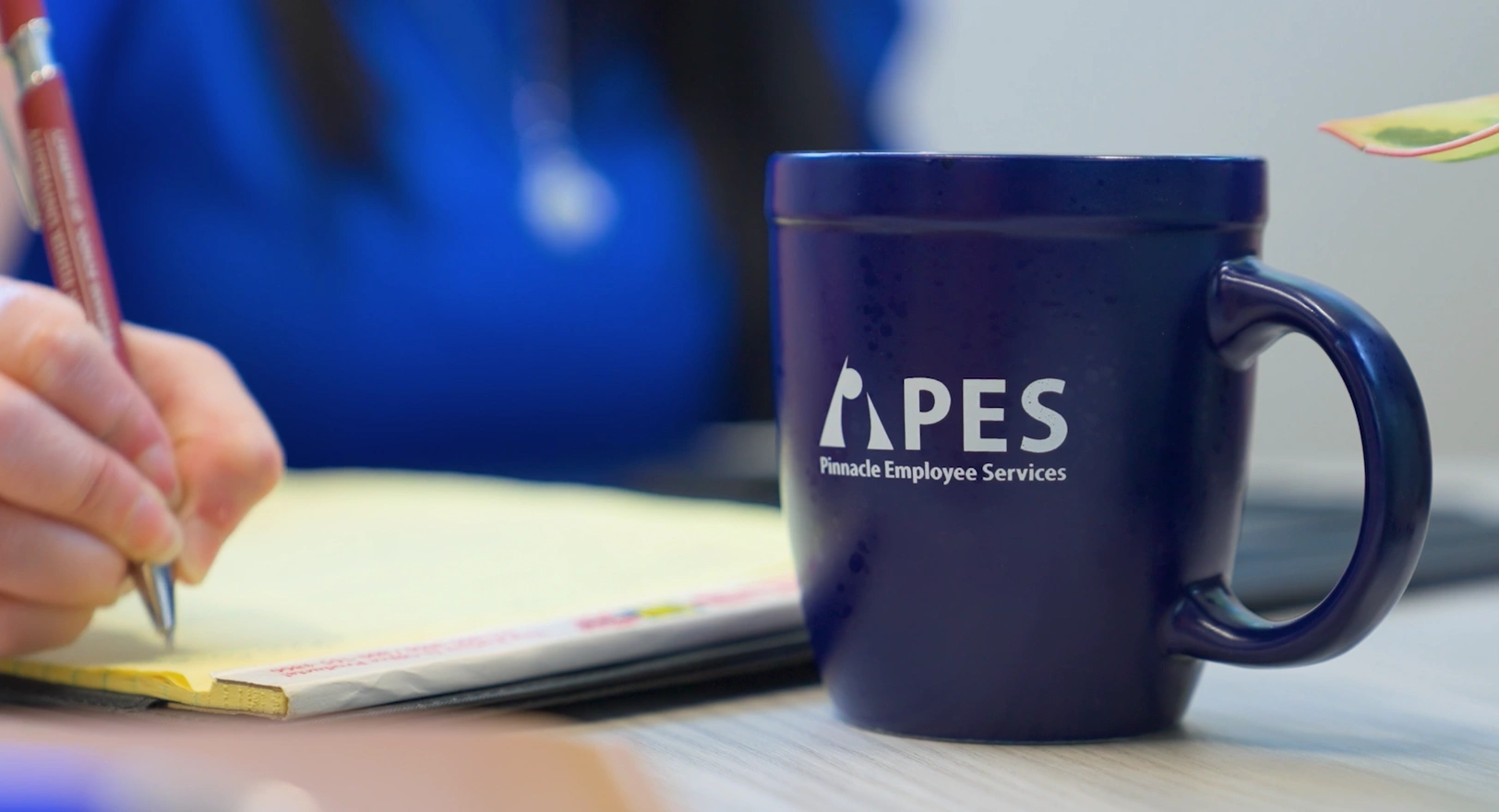 close up of PES mug and employee writing notes